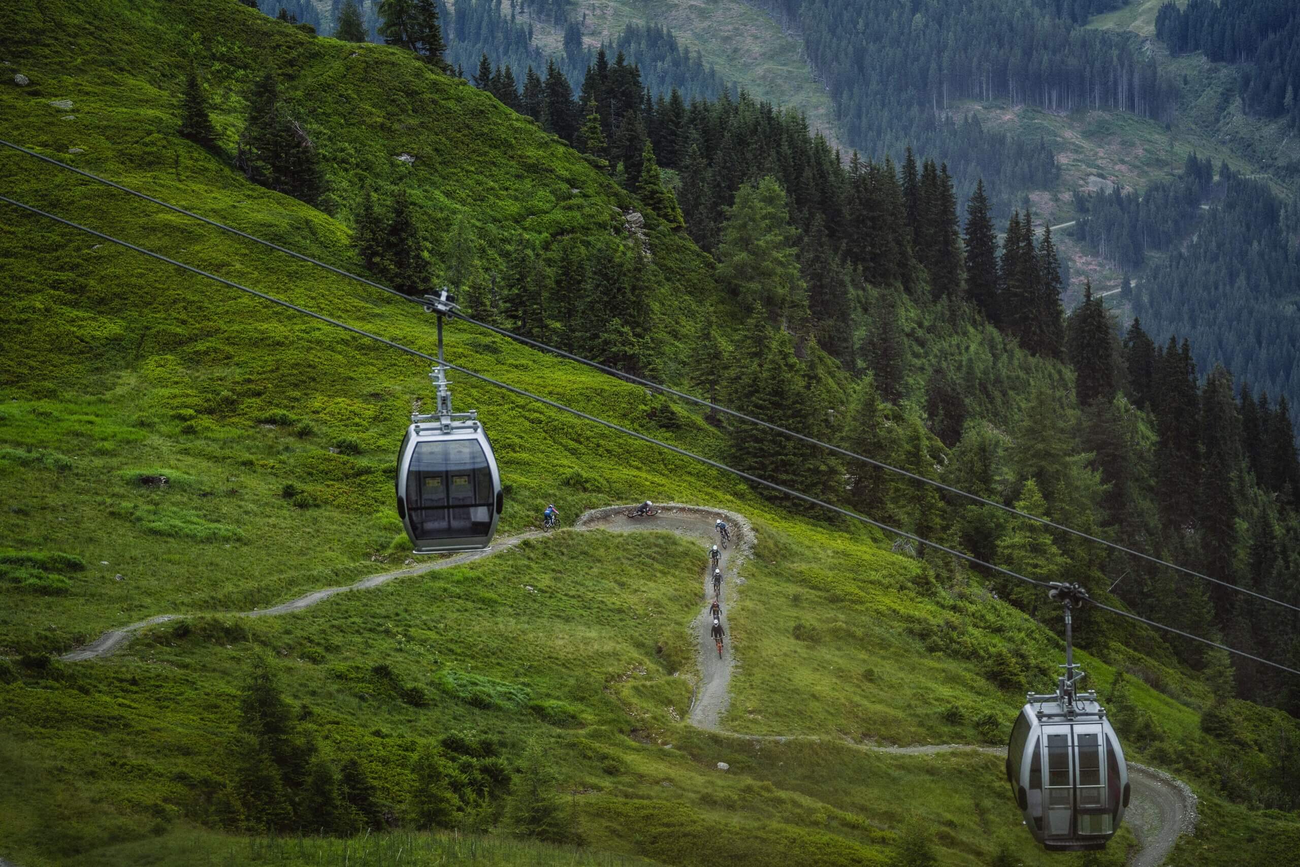 Gondeln und Radfahrer auf steilem grünen Bergpfad.