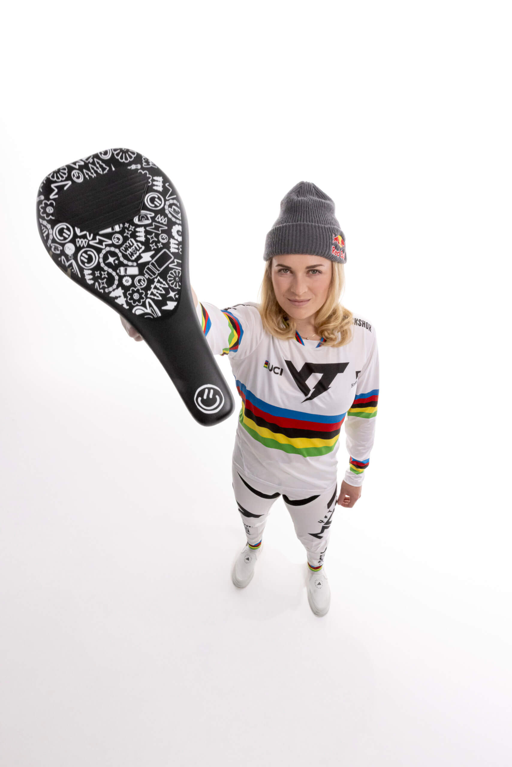 Frau im weißen Radsportanzug hält schwarzen Sattel mit Mustern.