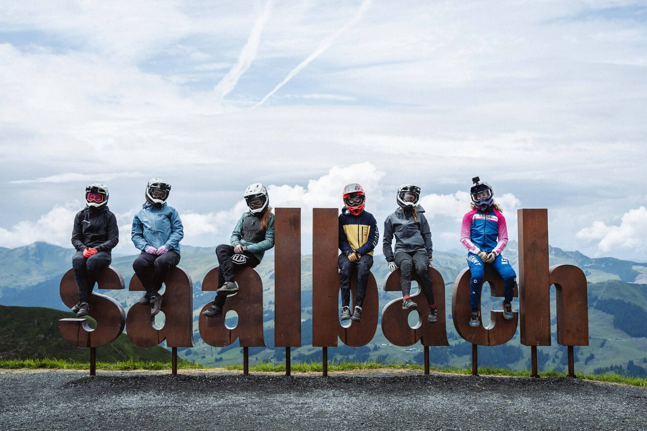 Sechs Mountainbiker auf Saalbach-Buchstaben in den Bergen.