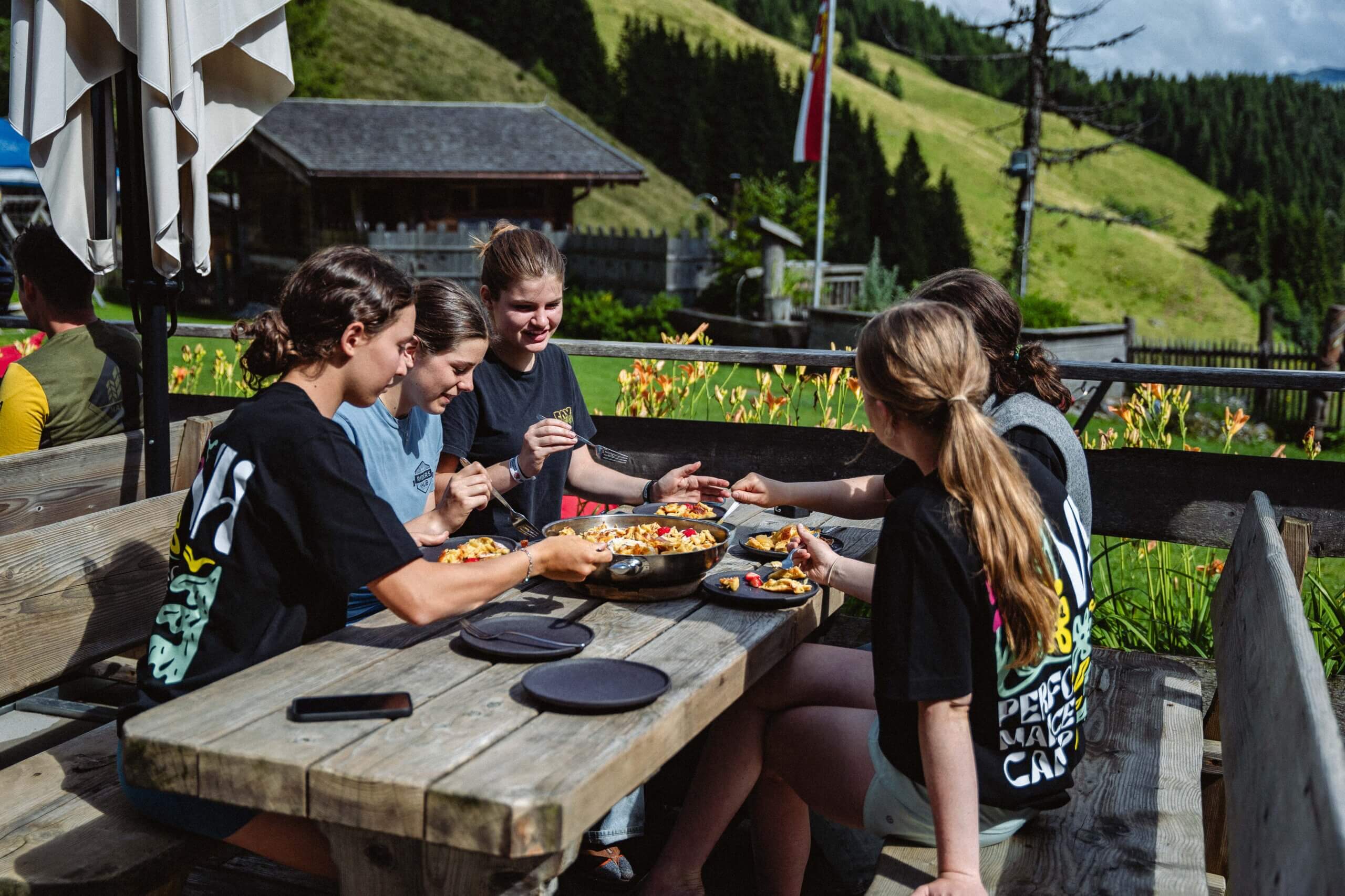 Gruppe isst draußen Kaiserschmarrn mit Bergblick.